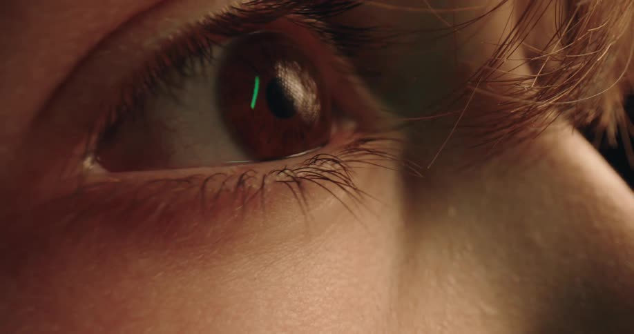 An extreme closeup shows a persons brown eye opening slowly revealing the iris and pupil as he react to the warm light in a dark setting