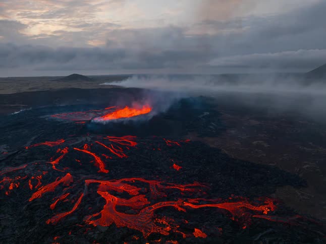 Lava fire lies across the base of the volcanic mountain glowing in bright molten streaks as thick smoke rises into the air