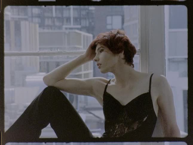 Woman sitting by a window rests her hand on her forehead and looks outside indoors