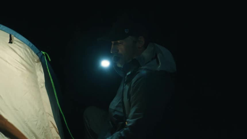 Man adjusts the fabric of a tent in a dark environment using a headlamp