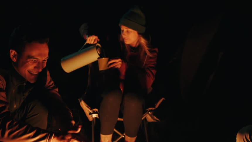 People are drinking and laughing at a campfire