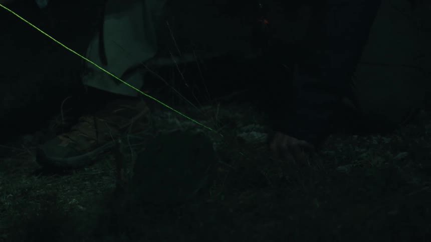 Man concentrates on a task involving a yellow cord while outdoors in the wilderness