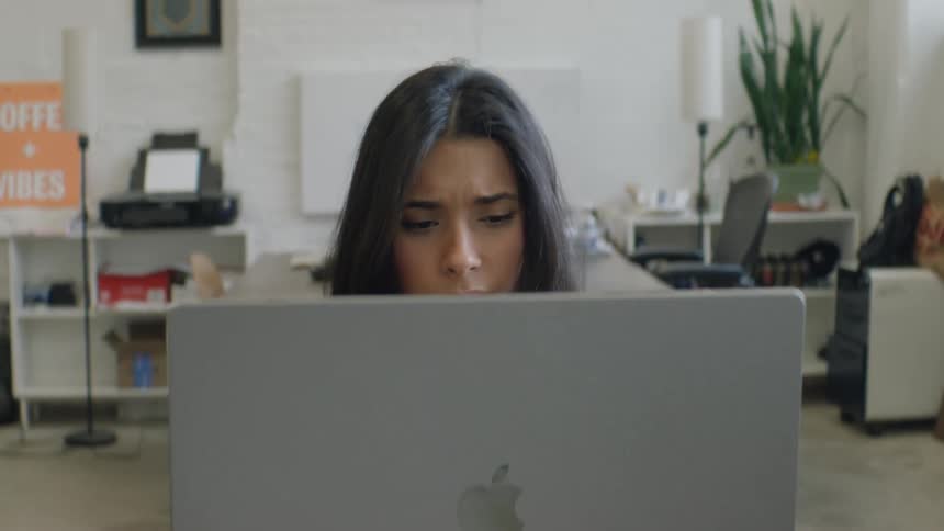 Young adult woman in an office sitting in front of an apple laptop indoors during day time