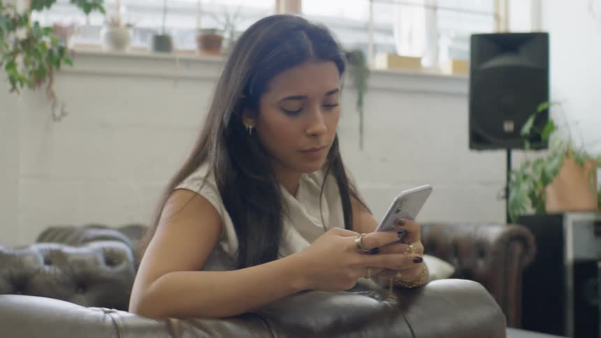 Young woman sitting on a couch texting on her phone