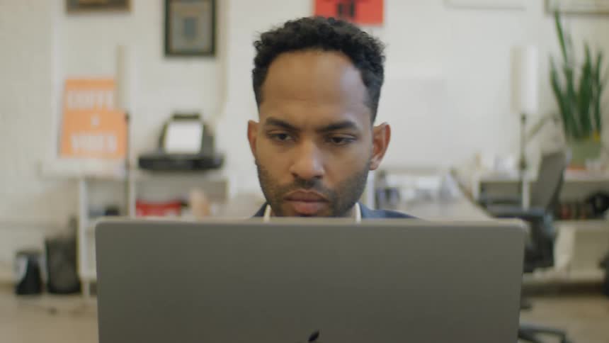 Man sits at a table typing on a laptop computer