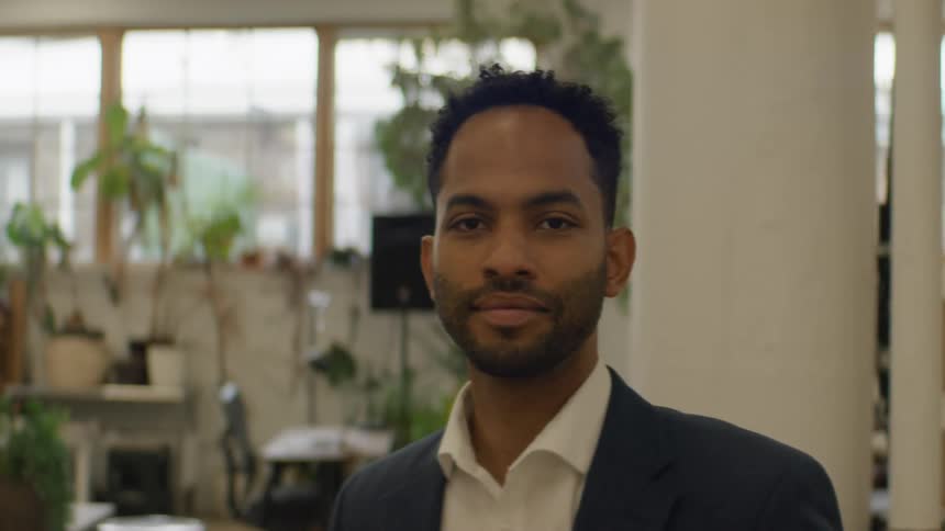 Man smiling in an office with plants and windows in the background