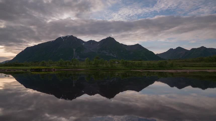 Clouds pass by above a lake and rugged mountains