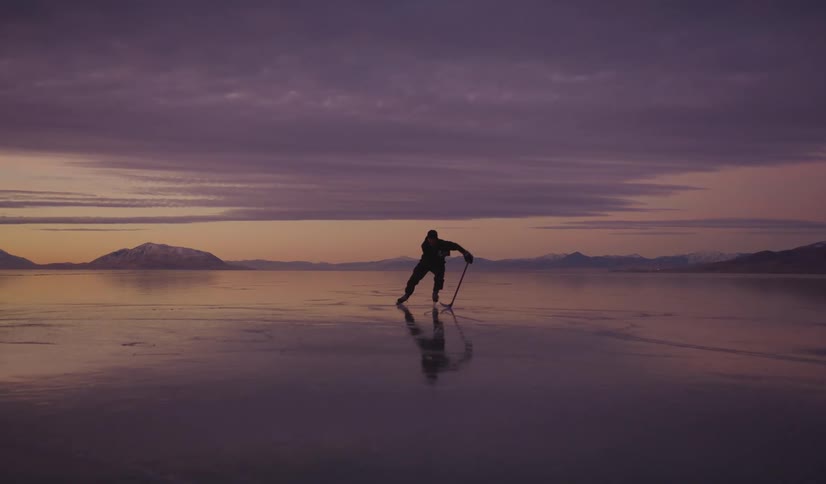 A man skates across a vast frozen lake at sunset while handling a hockey stick
