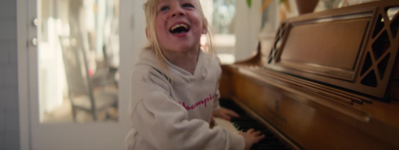 Girl smiles while playing a wooden piano indoors with natural light