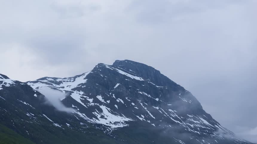 Clouds rolling on the side of snow capped mountain