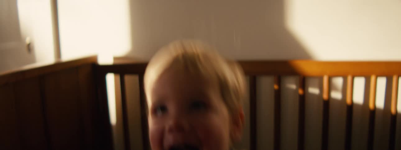 Young child smiles while jumping on the mattress in his crib during the daytime
