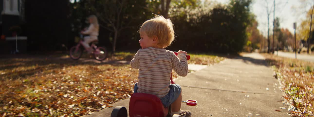 Two children ride bikes on the sidewalk