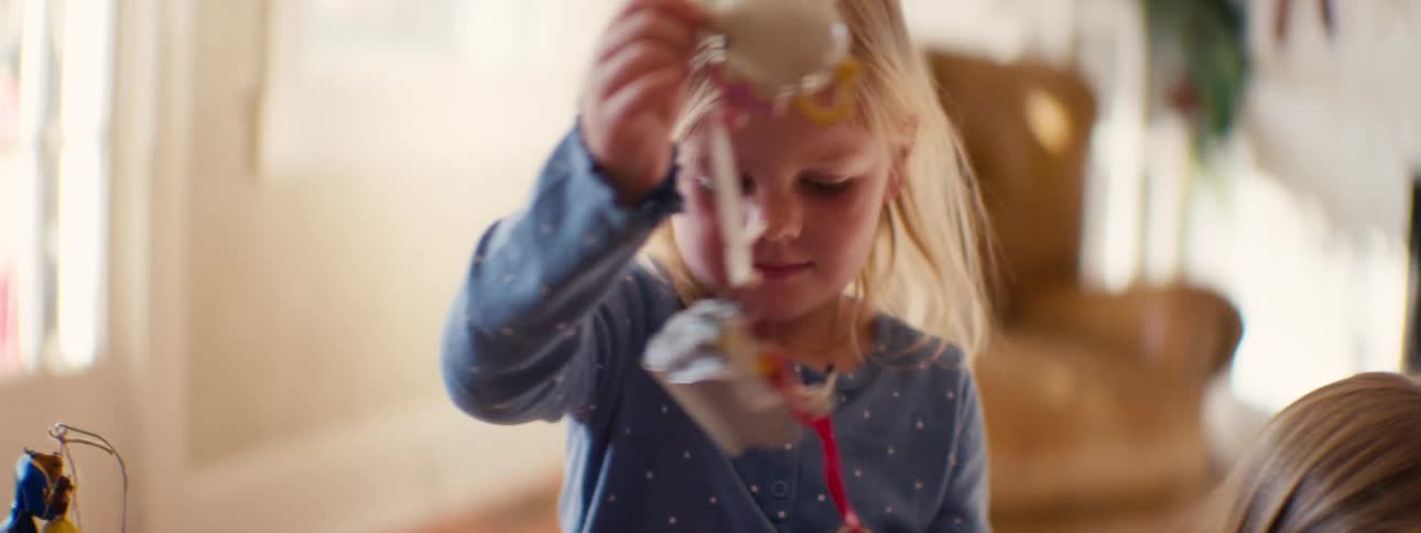 A young blonde girl in a blue shirt plays with a toy tea set indoors