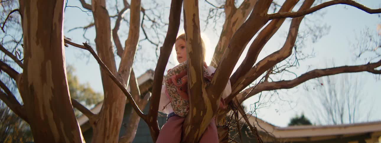 Little girl sitting among tree branches in a residential yard with houses in the background