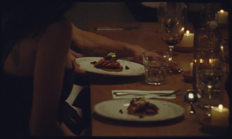 A server places a plate of food in front of a guest seated at a dimly lit wooden tablethe table is decorated with glowing candles wine glasses and water carafes creating a warm and intimate atmosphere