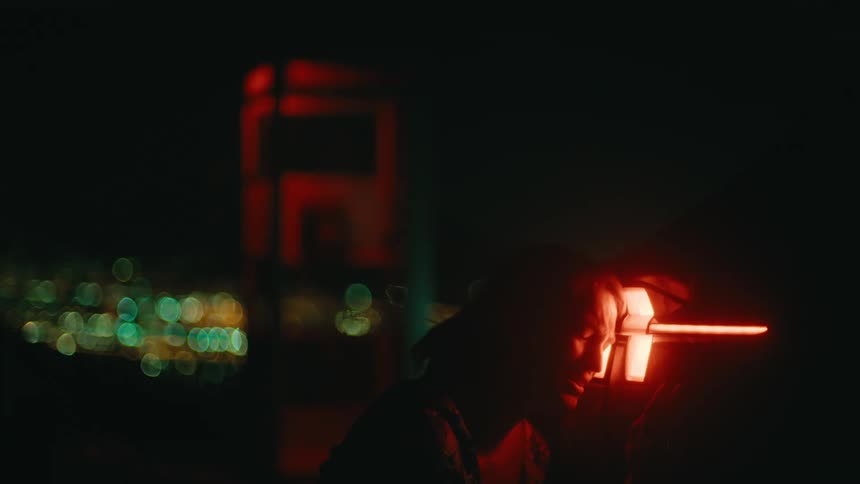 A person cries beneath a glowing red futuristic device at night with blurred city lights
