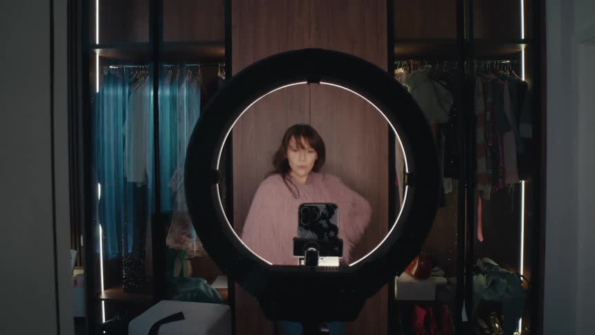 Woman stands in front of a phone mounted on a tripod with a ring light in a walkin closet