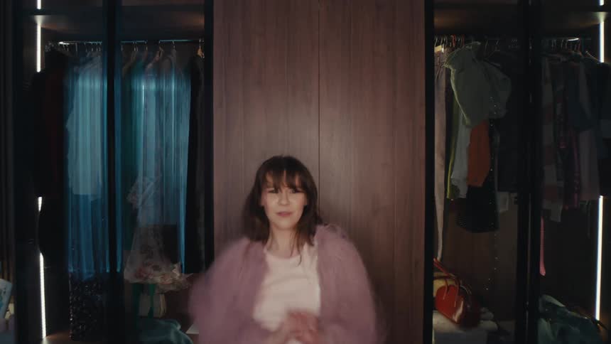 Woman dances in front of a phone on a tripod with a ring light in a walkin closet