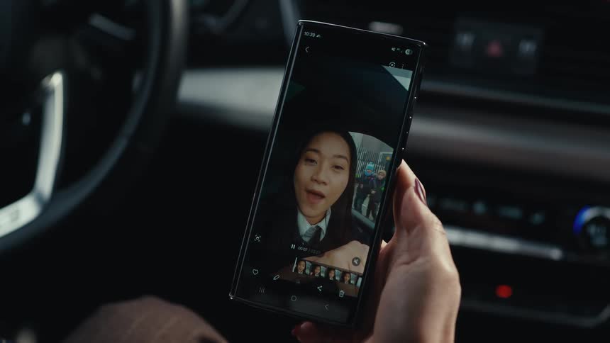 Person shown in a video call displayed on a smartphone screen held inside a car