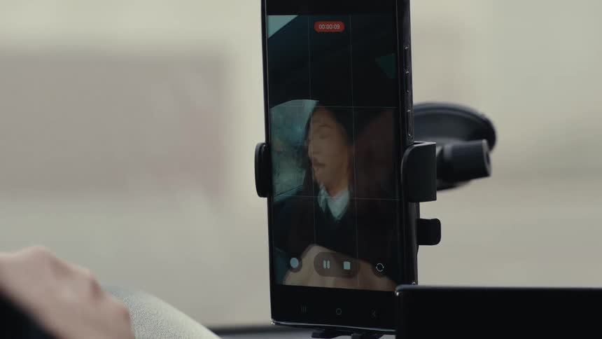 Person speaking during a video call displayed on a smartphone mounted on a car dashboard
