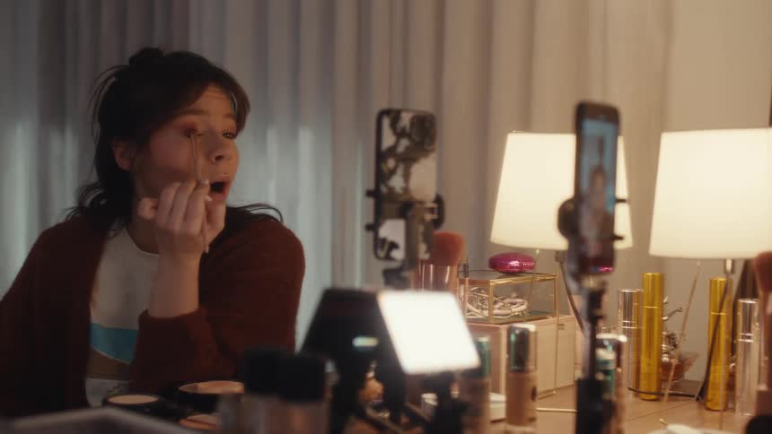 Young womans phone set up to take a selfie as she applies makeup to her face