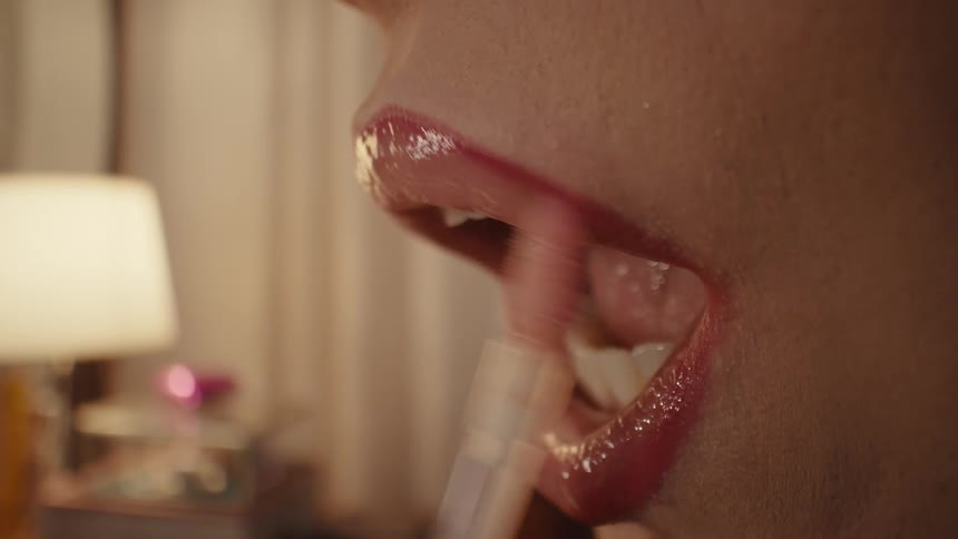 A close up shot shows a person applying pink lip gloss to their lips with an applicator