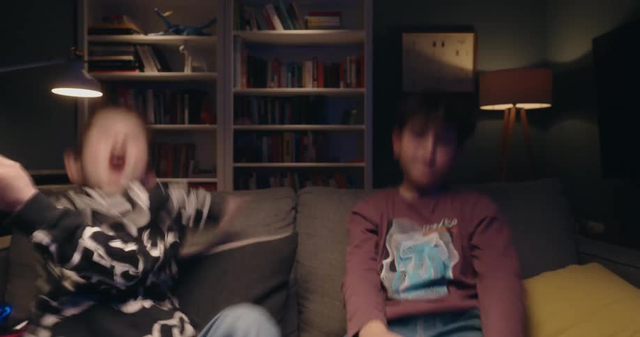 Two young boys excitedly play a video together and one celebrates winning