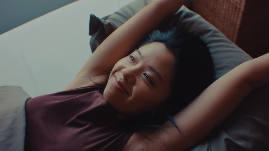 A woman smiles and stretches as she sits up in her bed