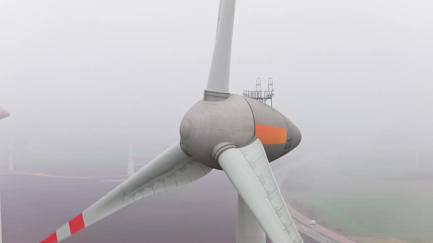 Turbine spinning on a wind farm as traffic moves on the road below