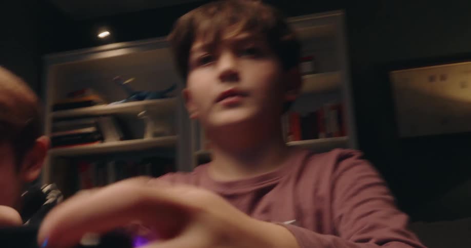 Children holding a video game controller while playing indoors with a bookshelf in the background