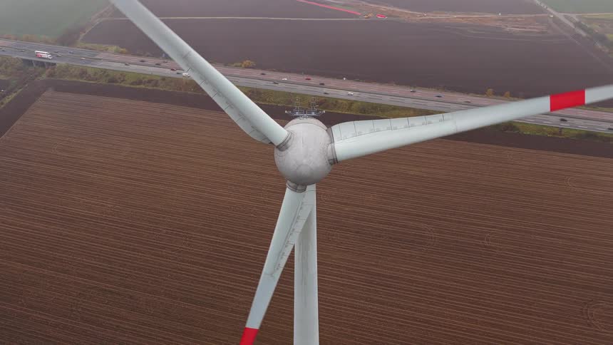 Wind turbine over a field next to a road with vehicle traffic outdoors during day time