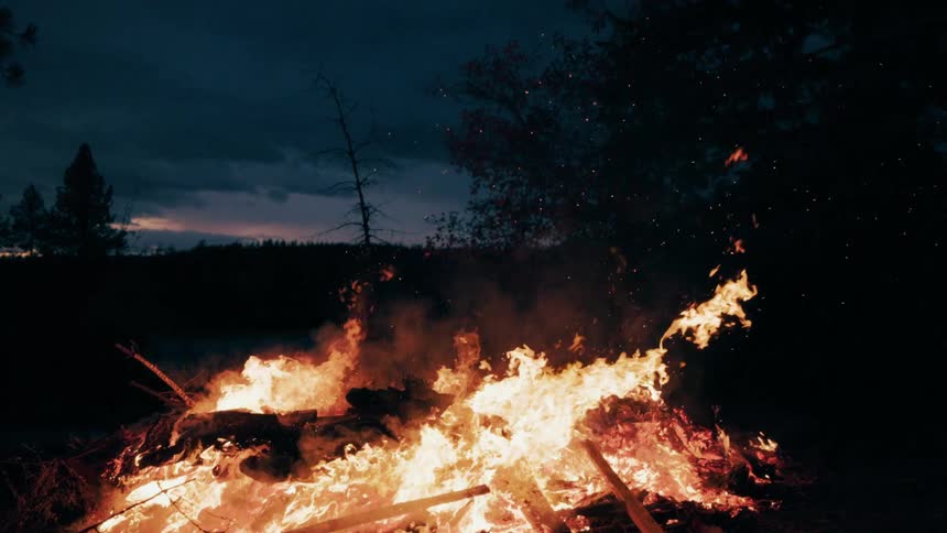 Outdoor bonfire with intense flames consuming wood at night
