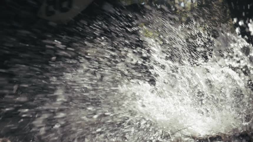 A mountain bike wheel splashes through a shallow stream in a forest in slow motion