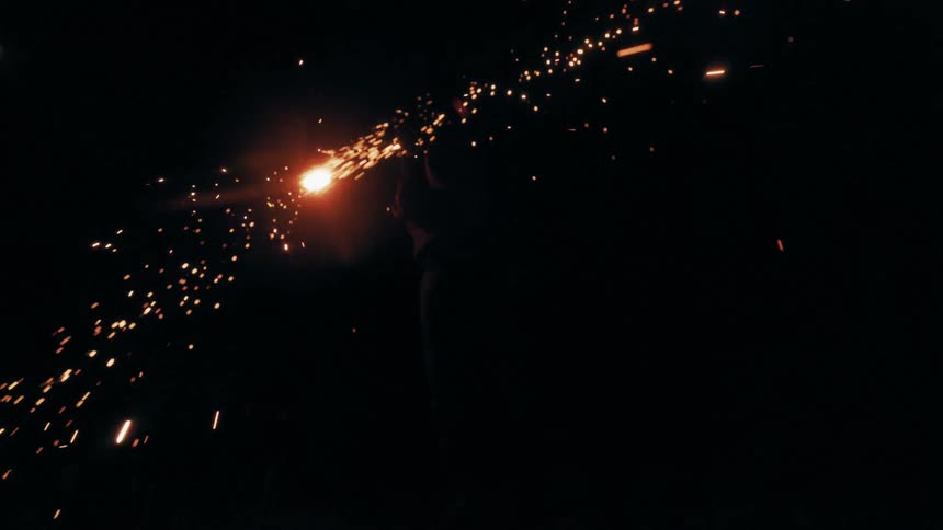 A man waves a sparkling light source in the darkness creating bright blurred light trails