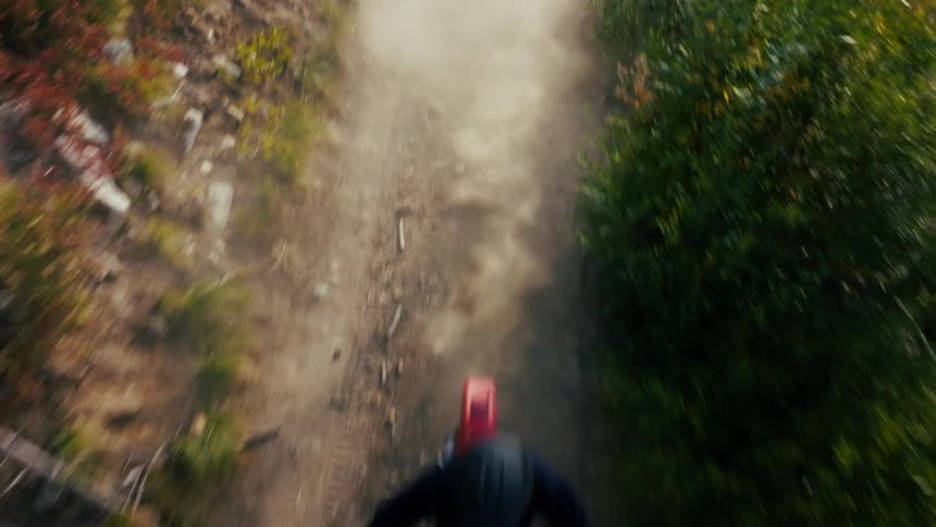 Biker wearing a helmet riding a motorcycle on a narrow dust road surrounded by vegetation outdoors during day time
