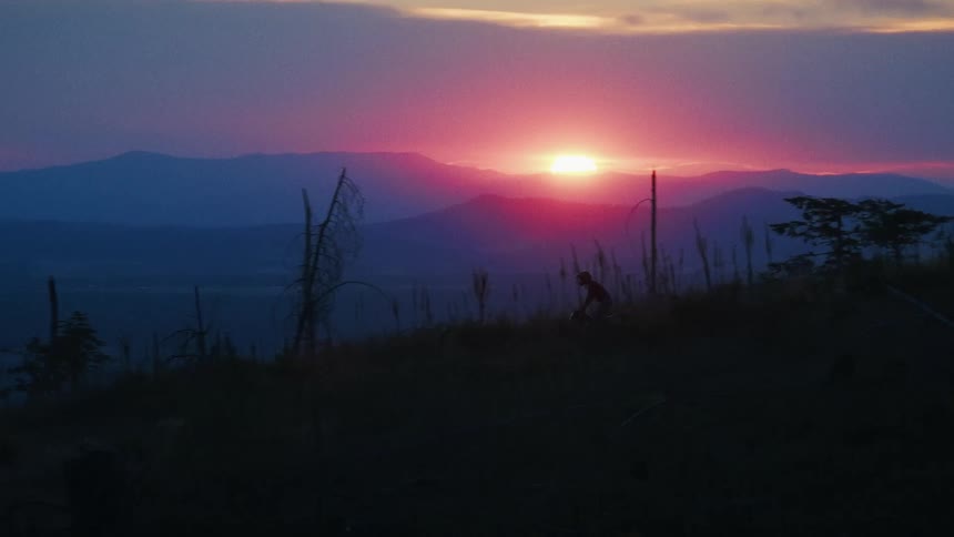A person on a motorcycle rides through a rural area near mountains
