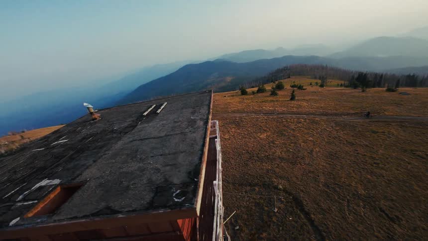 A man is flying a drone around a fire lookout on a mountain