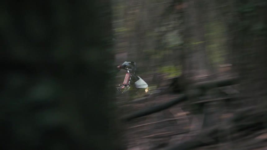 Motocross rider moving along a forest trail surrounded by dust seen through blurred trees