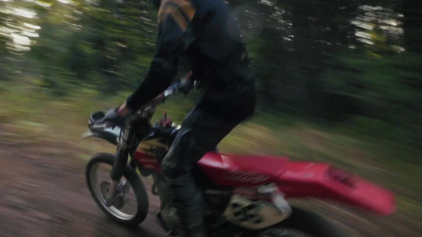 A helmeted dirt bike rider races down a forest trail motion blur and drifting dust capturing the speed and energy of the ride