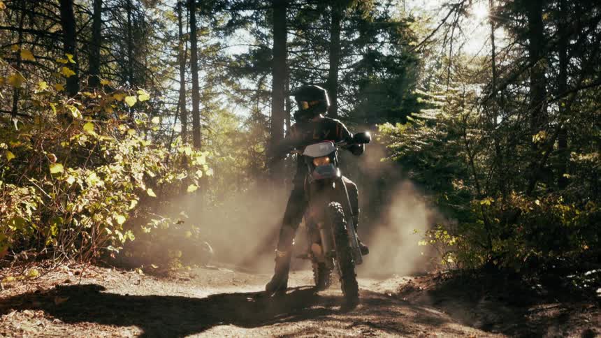A man on a motorcycle stops on a forest path before taking off again