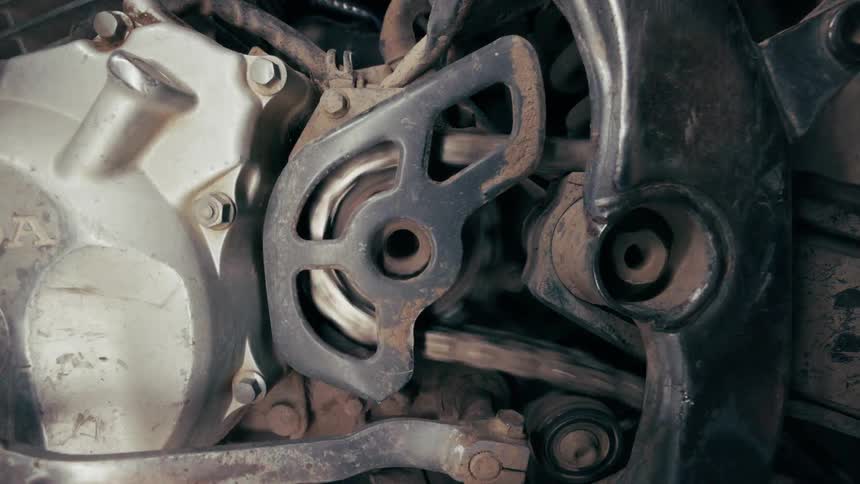 An extreme closeup shot shows the gritty mechanical details of a motorcycles engine and drive chainthe lighting shifts from a bright natural exposure to a dramatic shadowy highcontrast view of the metal components