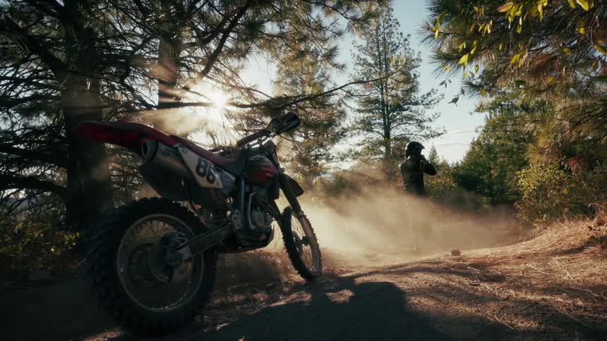 The man puts on his helmet and walks to the dirt bike