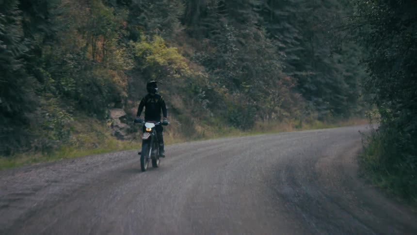 Motocross rider riding on a dirt road surrounded by dense forest
