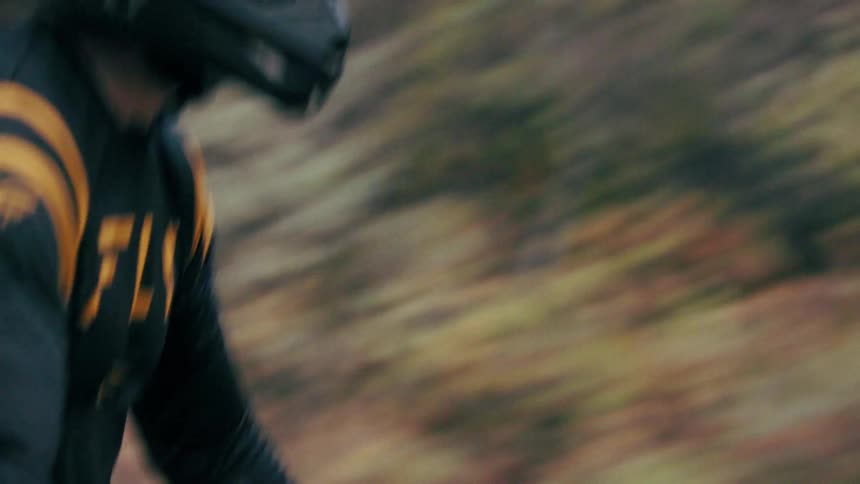 A helmeted dirt bike rider races down a forest trail with motion blur at times