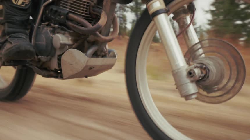 Wheel of a motorcycle in motion over a road surrounded by trees outdoors during day time