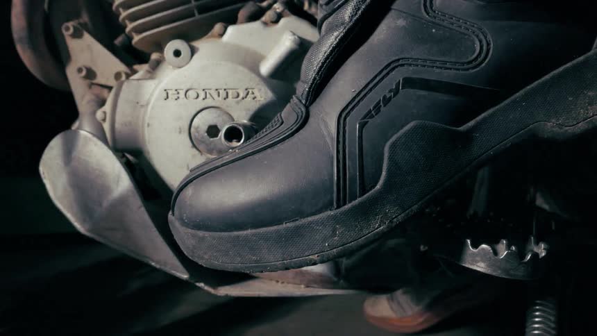 Rider boot resting on a honda motorcycle foot control in a mechanical closeup
