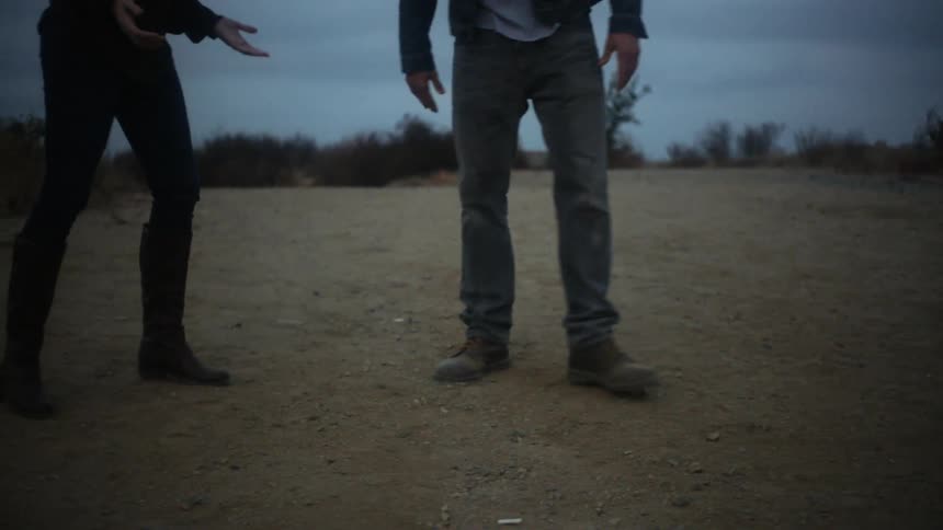 A man and woman are arguing on a patch of dirt outside
