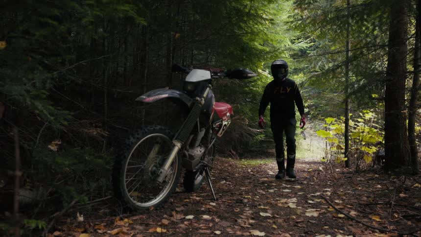The man walks over to his dirt bike on the trail