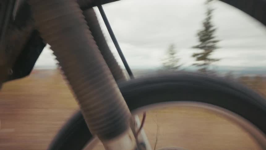 A motorcyclist rides at high speed down a dusty unpaved trail through a wooded area the camera follows closely behind the bike capturing the dust kicking up and the rider navigating the uneven terrain