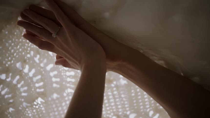 A woman rubs her hands on lace sheets